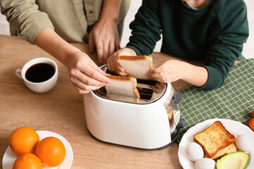 Little boy and his mother putting bread slices into toaster in kitchen, closeup