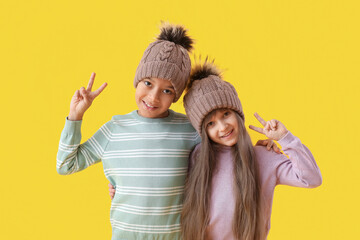 Cute little children in winter clothes showing victory gesture on color background