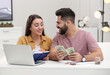 © New Africa - Happy young couple counting money at white table indoors