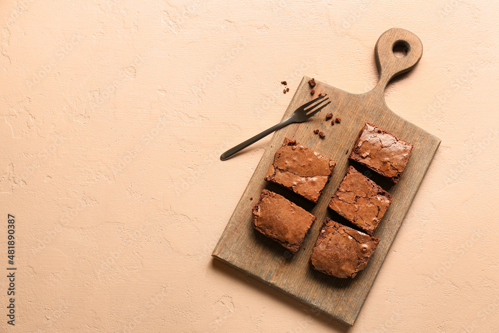 Wooden board with pieces of tasty chocolate brownie on beige background