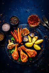 Wall Mural - Barbecue chicken drumsticks with potatoes and carrot on wooden table
