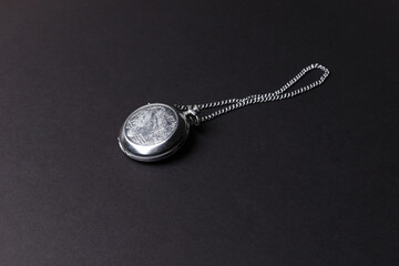 The concept of antiques. A silver vintage, retro watch with a chain lies on a black background. An engraved image of a bird on a retro watch. Side view.