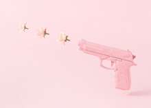 Pink Gun And Three Rose Flowers Bullets Against Pastel Pink Background. Creative Peace Concept.