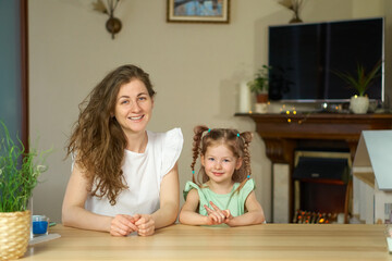 Portrait happy smile family. Mom and daughter at table look at cameras. two sisters laugh At home room and laugh. Place for text. childhood. Caucasian woman and girl in frame. Nanny child Babysitter.