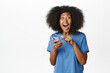 © Cookie Studio - Image of african american modern woman in blue t-shirt, reacting amazed and surprised at mobile phone app, announcement on smartphone, smiling happy and excited