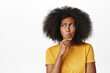 © Cookie Studio - Close up of african american woman deep thinking, looking hesitant away while standing in thoughtful pose, wearing yellow t-shirt, white background