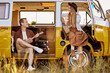 © Roman - joyous hipster couple playing guitar ukulele sing a song in yellow van, in nature, field in countryside. traveler traveling together with vintage mini van in camping tent. camper vacation outdoors
