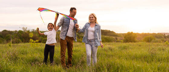 Wall Mural - Happy family father, mother and child daughter launch a kite on nature at sunset