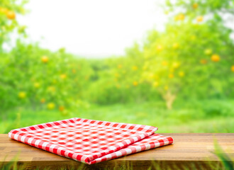 Red checked cloth on wood table top with blur of orange garden farm background.