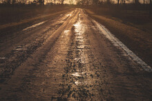 Dirty Sand And Gravel Road With Puddles In Sunset Golden Light