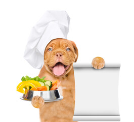 Poster - Happy puppy wearing a chef's cap  holds bowl of vegetables and empty list. isolated on white background
