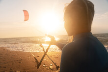 Sportswoman Woman Kitesurfer Holds Her Kite Over The Surface Of The Sea With Waves At Sunset. Space To Copy Water Sports. Kitesurf Instructor Looking At The Setting Sun And Kite