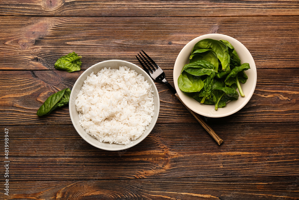 Bowl with tasty boiled rice and spinach on wooden background