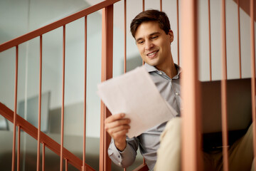 Smiling businessman reads documents while using laptop in the office.