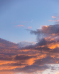 Wall Mural - Sliver of a crescent moon rising above colorful sunset clouds