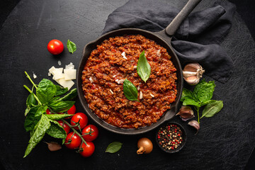 Wall Mural - classic italian bolognese sauce stewed in a pan with ingredients on black tile background, top view