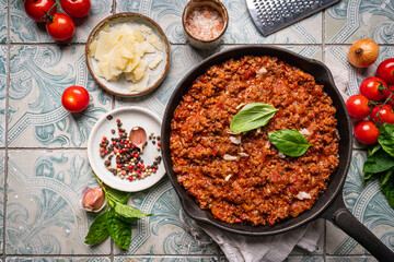 Wall Mural - classic italian bolognese sauce stewed in a pan with ingredients on tile background, top view