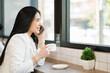 © thanmano - Asian businesswoman using technology. Professional woman is conversing on her phone while drinking coffee in a coffee shop. Working from anywhere