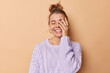 © wayhome.studio  - Happy carefree young woman makes face palm smiles broadly keeps eyes closed expresses positive emotions feels glad wears casual jumper isolated over beige background laughs at something funny