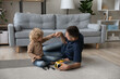 © fizkes - Happy cute small kid son bumping fists with caring millennial father, finishing repairing favorite toy car with screwdriver, having fun improving skills sitting on floor carpet together at home.