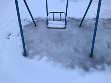 Children's Swing On The Playground Covered With Snow.