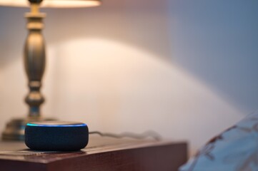 Personal assistant smart speaker on a wooden table with table lamp in a bed room and copy space for Editor's text