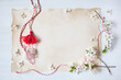 Flowering branches of cherry plum, red-white martenitsa with tassels and paper for text for the holiday of March 1, white wooden background.