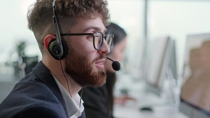 Close Up Portrait Man of a Technical Customer Support Specialist Talking on a Headset while Working on a Computer in a Call Center. Diverse group of workers talks on sale hotline. Busy seller at