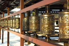 Rows Of Traditional Copper-metal Spinning Prayer Wheels With Tibetan Holy Sacred Mantras At Snowy Temple Complex At Winter, Spiritual Asian Culture Of Hindu And Buddhist Faith At Local Monastery