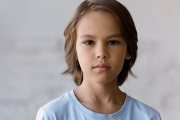 Serious pretty boy head shot portrait. Male school kid, schoolchild, young guy with neck-length brown hair looking at camera. Close up of face, front view. Childhood concept