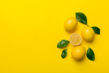 Many fresh ripe lemons with green leaves on colored background, top view, space for text