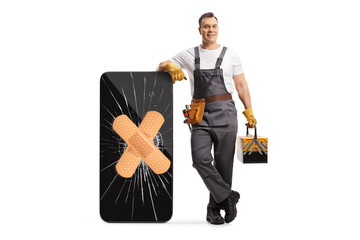 Wall Mural - Full length portrait of a repairman leaning on a smartphone with a cracked screen and adhesive bandage