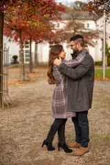 Wall Mural - Young european married couple with building behind dancing in autumn park