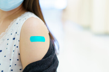 Happy Asian young woman wearing a protective face mask showing her vaccination spot on her arm.