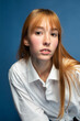 Closeup portrait of girl with red hair and white skin isolated on blue in shirt