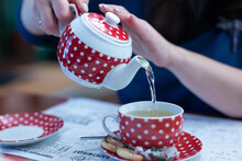 Women's Hands Pour Green Tea From A Teapot Into A Cup, Red Dishes With White Polka Dots