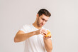 Portrait of dissatisfied young man with disgust picking bud of bad burger on white isolated background. Studio shot of handsome bearded male holding in hands unhealthy delicious hamburger.