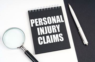 On a black and white surface lies a magnifying glass, a pen and a notepad with the inscription - Personal Injury Claims