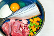 Natural dog food in bowl. Close-up  bowl of fresh raw meat, fish and vegetables on grey background