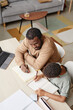 © Seventyfour - High angle portrait of caring father helping son with homework while studying at home, copy space