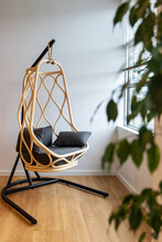 Comfortable, Wicker Chair Swing Basket Hangs From A Metal Frame In Front Of A Window With A Green Plant In Front