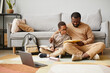 © Seventyfour - Full length portrait of African-American father and son sitting on floor while doing homework together, copy space