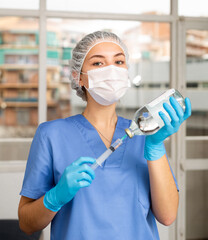 Wall Mural - Portrait of lady doctor with vial and syringe in her hands in professional protective clothing - medical mask and surgical cap