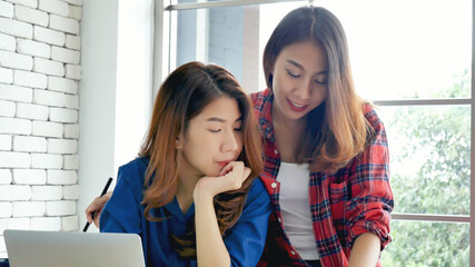 Canvas Print - Happiness two women working together confident team meeting in office desk. Team business partners working with computer laptop startup company. Asian colleague friendship at work with smiling face.