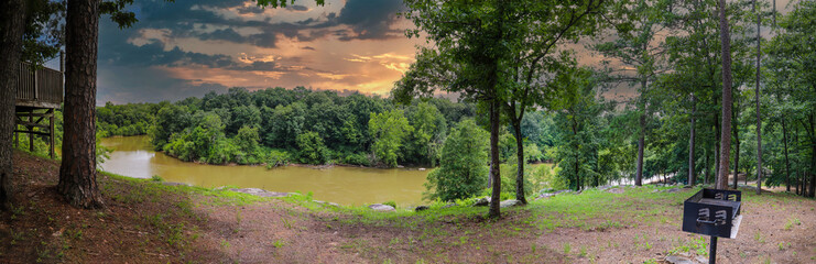 a stunning shot of t silky green waters of the Chattahoochee river with lush green trees on the banks of the river with powerful clouds at sunset at McIntosh Reserve Park in Whitesburg Georgia USA