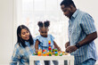 © Art_Photo - Portrait of happy love black family african american father and mother with little girl smiling activity learn and skill brain training play with toy build wooden blocks board education game at home