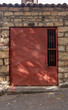 Red metal door with lattice closed on chain with lock in old stone wall. Vertical photo.