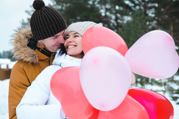 Wall Mural - A man and a woman in love on an outdoor date in winter in the snow with a gift of pink and red balloons in the shape of a heart. Valentine's Day, love, happy couple in love on a walk