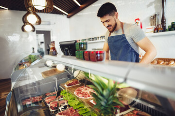 Poster - Young man butcher arranging meat products in display case of butcher shop