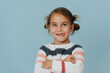 Perky little girl in sweater standing with hands crossed, sticking out tongue